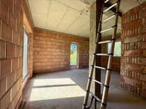 Wnętrze pokoju w stanie surowym – ceglane ściany i drabina, dom w budowie Mauryców koło Łasku