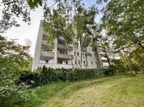 Widok zewnętrzny bloku z balkonami wśród drzew, Łódź-Olechów, tereny zielone wokół