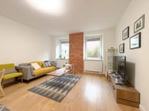 Salon z drewnianą podłogą, żółtą sofą, ceglaną ścianą akcentującą i jadalnią – Tuwima Łódź