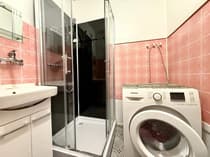 Łazienka z różowymi kafelkami, kabiną prysznicową i pralką automatyczną