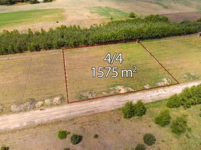 Widok z lotu ptaka na prostokątną działkę zaznaczoną na czerwono, oznaczoną numerem 4/4 o powierzchni 1575 m². Działka na sprzedaż Skotniki - łódzkie znajduje się przy drodze gruntowej, graniczy z drzewami i otoczona jest otwartymi terenami trawiastymi. biuro nieruchomości