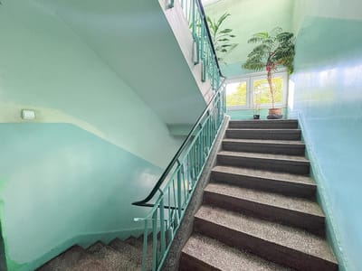 Klatka schodowa w budynku w łódzkim Śródmieściu, z jasnozielonymi ścianami, metalowymi poręczami i roślinami doniczkowymi przy oknie na podeście, wpuszczającymi naturalne światło - idealne do zachęcającego mieszkania na sprzedaż. biuro nieruchomości