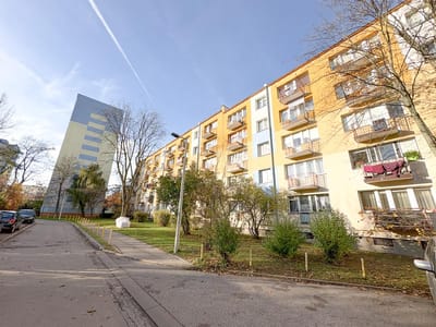 Szerokokątny widok na ulicę mieszkalną w łódzkiej dzielnicy Retkinia, na której znajduje się żółto-biały budynek mieszkalny z balkonami - idealny dla osób poszukujących mieszkania na sprzedaż - drzewa bez liści i nowoczesny szklany budynek pod błękitnym niebem. biuro nieruchomości