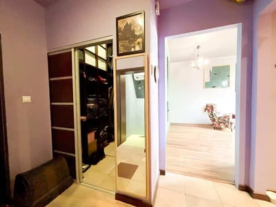 Przedpokój z fioletowymi ścianami, lustrzanymi drzwiami do szafy, lustrem na ścianie i oprawionym obrazem powyżej. Za drzwiami znajduje się jasny pokój z drewnianą podłogą i fotelem w kwiaty. biuro nieruchomości