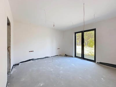Pusty, niedokończony pokój z białymi ścianami, odsłoniętym okablowaniem z sufitu, gniazdkami elektrycznymi w ścianach i dużymi szklanymi drzwiami prowadzącymi na zewnątrz - rzut oka na potencjał, jaki oferuje ten dom na sprzedaż Radomsko - Wygoda. Zakurzona podłoga czeka na Twoją wizję. biuro nieruchomości