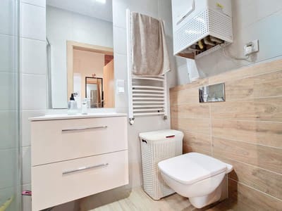 Nowoczesna łazienka w mieszkaniu na sprzedaż Łódź Śródmieście Tuwima, z pływającą białą toaletką, toaletą naścienną, boazerią z jasnego drewna, wiklinowym koszem na śmieci, podgrzewanym wieszakiem na ręczniki, podgrzewaczem wody, dużym lustrem i jasnymi neutralnymi odcieniami. biuro nieruchomości