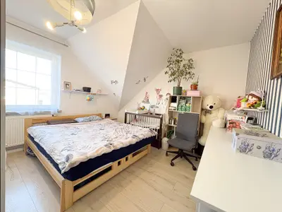 Duża sypialnia na poddaszu z tapicerowanym łóżkiem i tapetą w paski