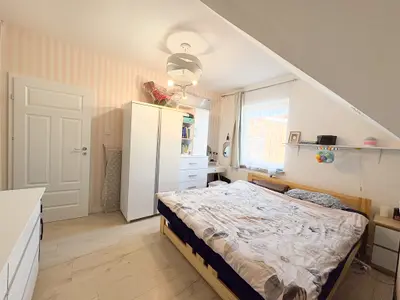 Sypialnia z podwójnym łóżkiem i szafą na tle różowej tapety w paski