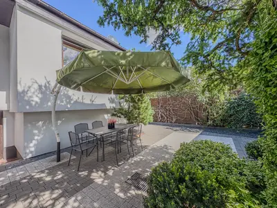 Taras z zielonym parasolem ogrodowym i zestawem krzeseł metalowych