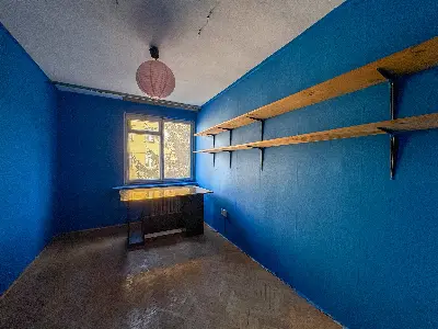 Pokój z niebieskimi ścianami i drewnianymi półkami w mieszkaniu na Bałutach