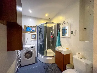 Łazienka z kabiną prysznicową, pralką i ciemnymi płytkami na Polesiu