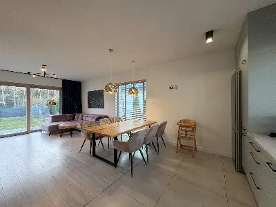 Jadalnia z drewnianym stołem i złotymi lampami nad nim, kuchnia w tle