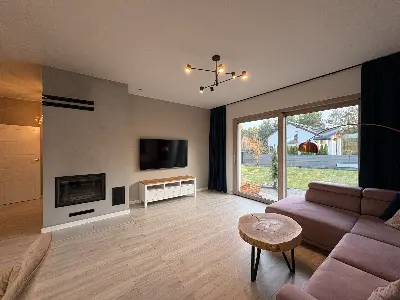 Salon z telewizorem i kominkiem, fioletowa sofa, widok na ogród przez przeszklone drzwi