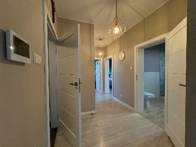 Korytarz z białymi drzwiami, złotą lampą i panelem domofonu