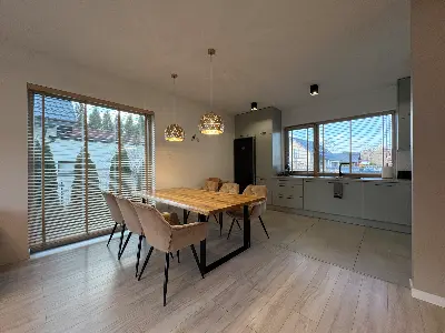 Jadalnia z drewnianym stołem przy oknie z żaluzjami i kuchnia otwarta