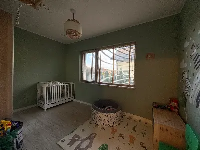 Pokój dziecięcy z zielonymi ścianami, łóżeczkiem niemowlęcym i matą do zabawy