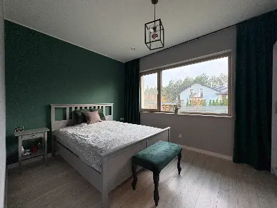 Sypialnia z ciemnozieloną ścianą akcentową i białym łóżkiem na parterze