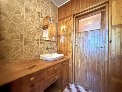 Łazienka z drewnianą szafką pod umywalką, kamienną mozaiką i przeszklonymi drzwiami