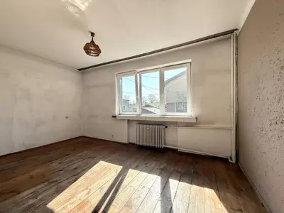 Nieumeblowany pokój z parkietem i oknem z grzejnikiem — wymaga odświeżenia
