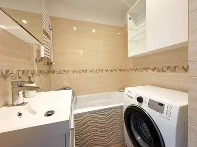 Łazienka z wanną, pralką i beżowymi kaflami w mieszkaniu na Bałutach w Łodzi