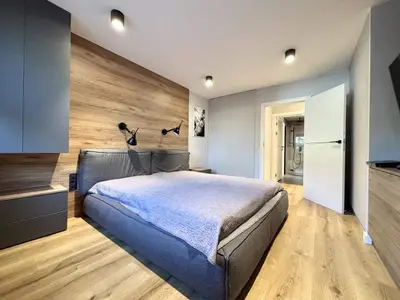 Sypialnia z drewnianą ścianą za łożem, wbudowaną szafą i wejściem do łazienki