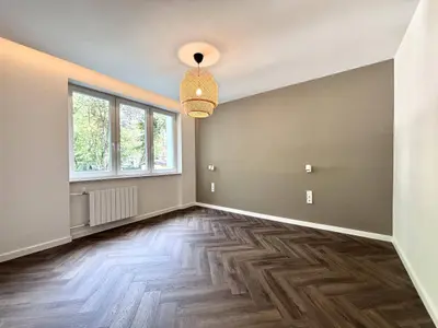 Jasny pokój z parkietem w jodełkę, szarą ścianą i widokiem na zieleń przez duże okno