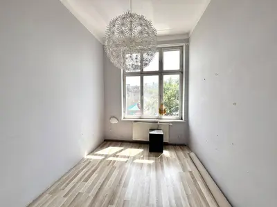 Pusty pokój z wysokim sufitem, dużym oknem i żyrandolem – kamienica w centrum Łodzi