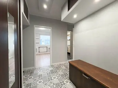 Przedpokój ze wzorzystą podłogą z płytek, szafkami z ciemnego drewna i przejściem do pokoju.