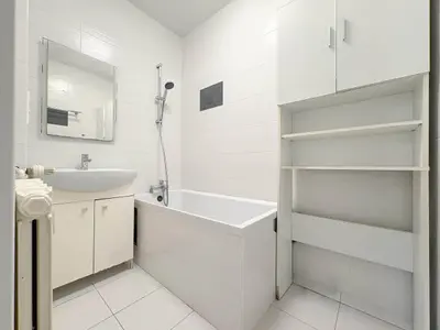 Biała łazienka z wanną, prysznicem, umywalką, lustrem i otwartymi półkami po prawej stronie.