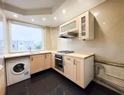 Kuchnia z jasnymi szafkami, kuchenką gazową, pralką i dużym oknem z widokiem na zewnątrz.