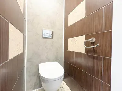 Toaleta z podwieszanym WC i brązowymi płytkami z beżowymi kwiatowymi akcentami.