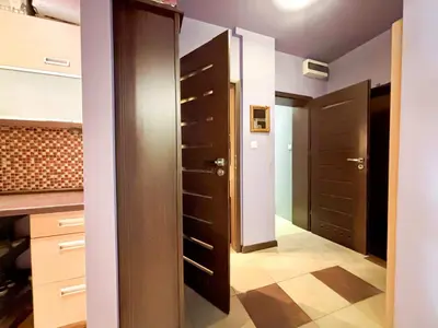 Korytarz z jasnofioletowymi ścianami, kafelkową podłogą i ciemnobrązowymi drzwiami do pokoi