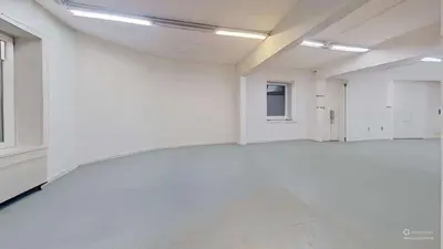 Przestronna sala z białymi ścianami, szarą posadzką i lampami sufitowymi — kamienica Bałuty