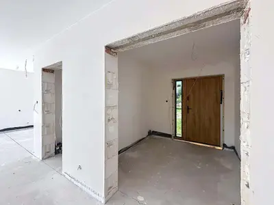 Przedsionek w stanie surowym z drewnianymi drzwiami wejściowymi i otwartymi przejściami między pomieszczeniami.