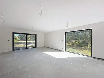 Przestronny pokój w stanie surowym z betonową podłogą i dużymi przeszklonymi drzwiami na ogród.