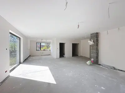 Duże niewykończone wnętrze z betonową podłogą, oknem i odsłoniętym filarem z pustaków.