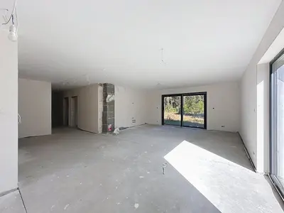 Przestronny pokój deweloperski z betonową podłogą, filarem i przeszklonymi drzwiami na ogród.