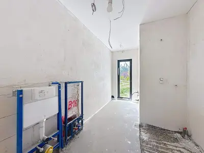 Pomieszczenie łazienki w budowie z zamontowanym stelażem WC i betonową podłogą.