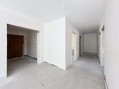 Korytarz w stanie surowym z drewnianymi drzwiami wejściowymi i widokiem na ciąg pomieszczeń.