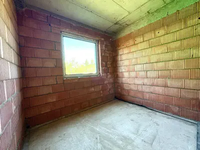 Mały pokój w stanie surowym z oknem – ceglane ściany, posadzka betonowa, dom Mauryców