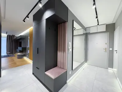 Przedpokój z czarną zabudową garderoby i różowym aksamitnym siedziskiem