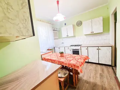 Kuchnia z zielonymi ścianami, białymi szafkami, kuchenką gazową i stołem z czerwonym obrusem.
