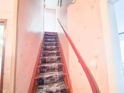 Strome schody z wzorzystym dywanem i czerwoną drewnianą poręczą prowadzące na piętro.