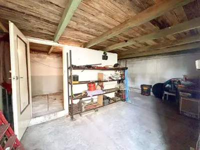 Piwnica lub garaż z drewnianym stropem, metalowymi regałami i narzędziami na betonowej podłodze.