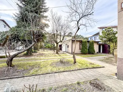 Ogród z wybrukowaną ścieżką, drzewami bez liści i widokiem na garaż oraz domy sąsiednie.