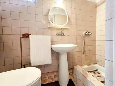 Łazienka z różowymi kafelkami, umywalką na postumencie, wanną, prysznicem i grzejnikiem.