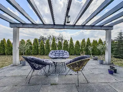 Taras pod pergolÄ z fotelami ogrodowymi i Å¼ywopÅotem z tuj we Wronowicach