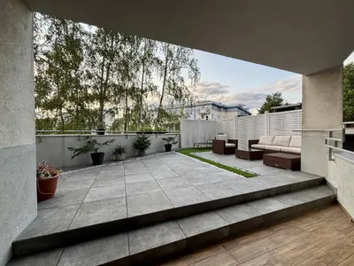 Przestronny taras przy parterze z meblami wypoczynkowymi, ogrodem i białym ogrodzeniem