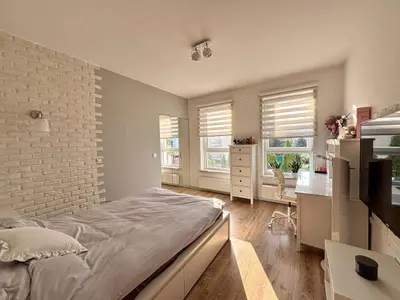 Duża sypialnia z łóżkiem, biurkiem, ceglastą ścianą dekoracyjną i dwoma oknami