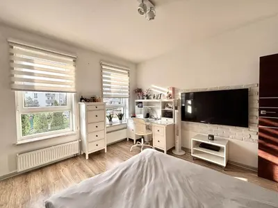 Jasna sypialnia z łóżkiem, biurkiem, telewizorem na ścianie i cegłą dekoracyjną